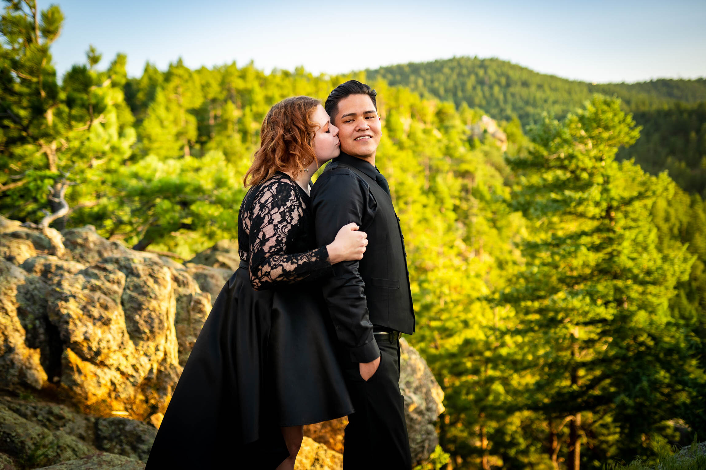 Engaged couple embraces for a portrait on a rocky ledge overlooking the mountains during golden hour, Engagement Session, Engagement Photos, Engagement Photos Inspiration, Engagement Photography, Engagement Photographer, Summer Engagement Photos, Mountain Engagement Photos, Lost Gulch Overlook engagement session, Lost Gulch Overlook engagement photos, Lost Gulch Overlook engagement photography, Lost Gulch Overlook engagement photographer, Lost Gulch Overlook  engagement inspiration, Boulder engagement session, Boulder engagement photos, Boulder engagement photography, Boulder engagement photographer, Boulder engagement inspiration, Colorado engagement session, Colorado engagement photos, Colorado engagement photography, Colorado engagement photographer, Colorado engagement inspiration