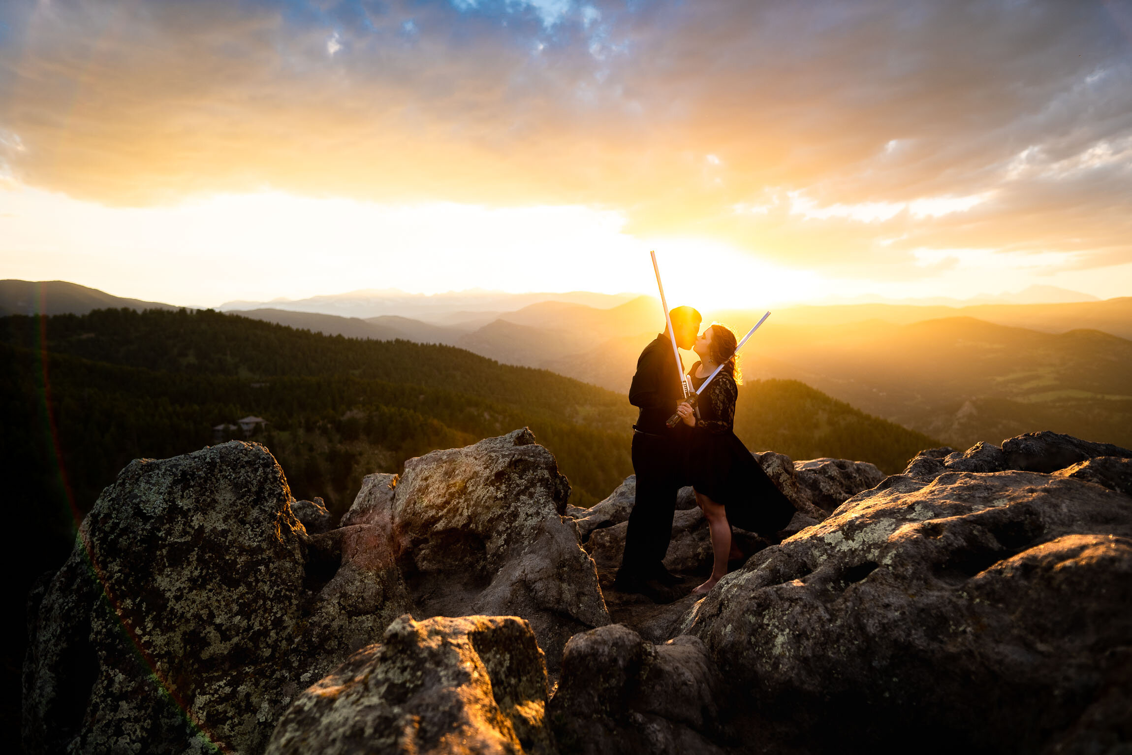 Engaged couple kisses while holding their light sabers on a rocky ledge overlooking the mountains during golden hour and sunset, Engagement Session, Engagement Photos, Engagement Photos Inspiration, Engagement Photography, Engagement Photographer, Summer Engagement Photos, Mountain Engagement Photos, Lost Gulch Overlook engagement session, Lost Gulch Overlook engagement photos, Lost Gulch Overlook engagement photography, Lost Gulch Overlook engagement photographer, Lost Gulch Overlook  engagement inspiration, Boulder engagement session, Boulder engagement photos, Boulder engagement photography, Boulder engagement photographer, Boulder engagement inspiration, Colorado engagement session, Colorado engagement photos, Colorado engagement photography, Colorado engagement photographer, Colorado engagement inspiration