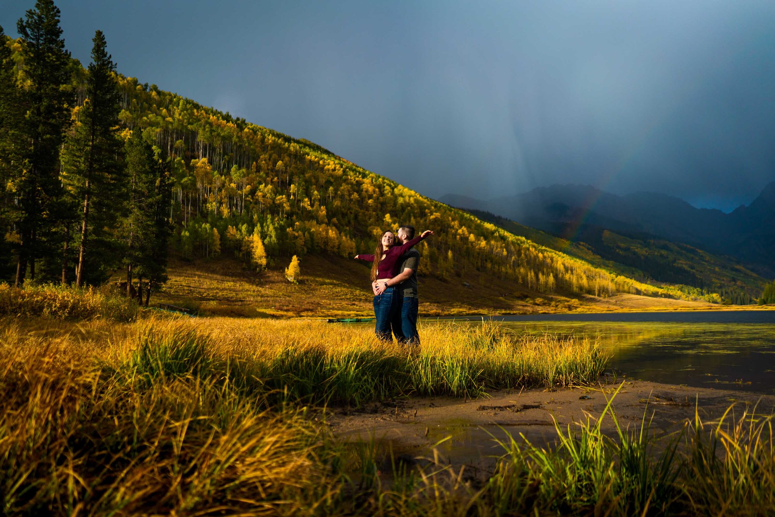 Engaged couple embraces for a portrait during a rainstorm with a double rainbow behind them arching over Piney Lake, Engagement Session, Engagement Photos, Engagement Photos Inspiration, Engagement Photography, Engagement Photographer, Fall Engagement Photos, Mountain Engagement Photos, Piney River Ranch engagement photos, Vail engagement session, Vail engagement photos, Vail engagement photography, Vail engagement photographer, Vail engagement inspiration, Colorado engagement session, Colorado engagement photos, Colorado engagement photography, Colorado engagement photographer, Colorado engagement inspiration